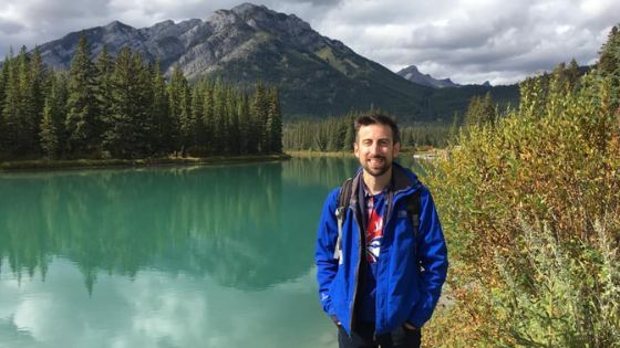 Photograph of Coeliac Man stood next to a river in front of a mountain